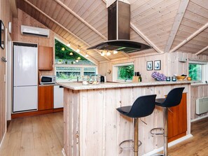 A wooden interior with a kitchen area featuring a refrigerator, microwave, and bar stools. - 4 Star Holiday Home in Oksbol (Oksbol)