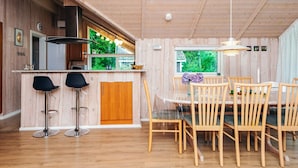 Un interior de madera con una zona de cocina, una mesa de comedor con sillas y un espacio con taburetes de bar.