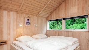 Un dormitorio con paneles de madera, una cama, dos lámparas fijadas a la pared, una ventana con vistas a la vegetación y una obra de arte enmarcada en la pared.