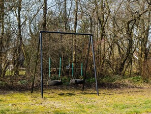 A swing set in a wooded area with bare trees and a grassy ground. - 4 Star Holiday Home in Oksbol (Oksbol)