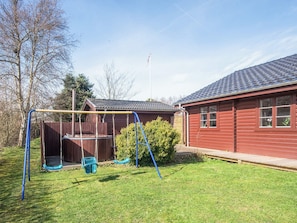A residential backyard with a swing set, a wooden deck, and a red house with a tiled roof. - 4 Star Holiday Home in Tarm (Tarm)