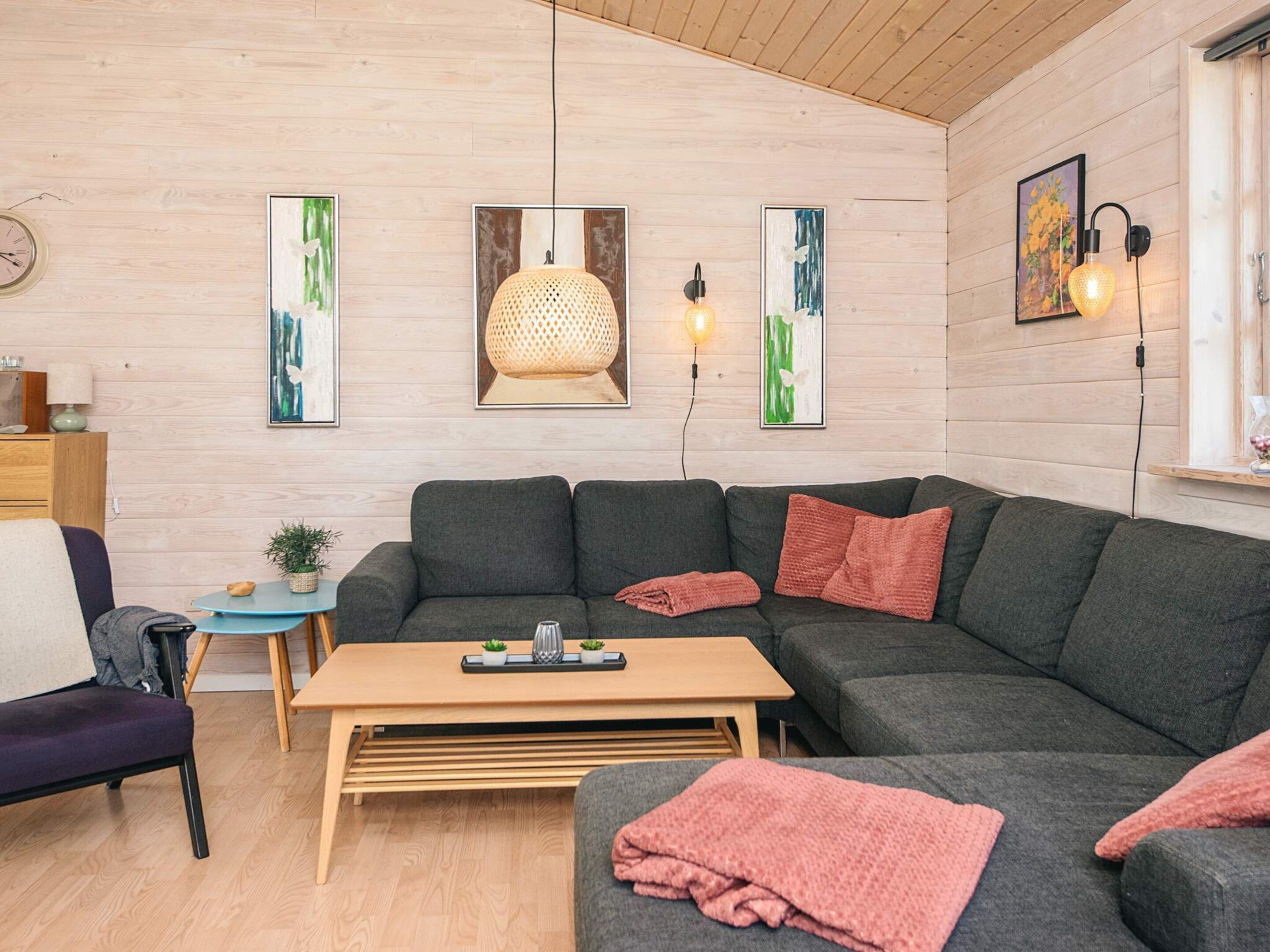 A modern living room with a grey sectional sofa, a wooden coffee table, a small round table with a plant, and artwork on the walls.