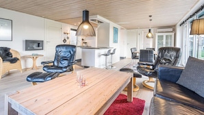 A modern living room with a wooden ceiling, leather sofas, a wooden coffee table, and a kitchen area in the background. - 5 Person Holiday Home in Blavand (Blavand)