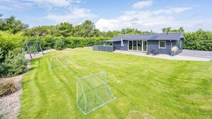 A residential property with a well-maintained lawn, a small house with a porch, and a fenced yard. - 5 Person Holiday Home in Blavand (Blavand)