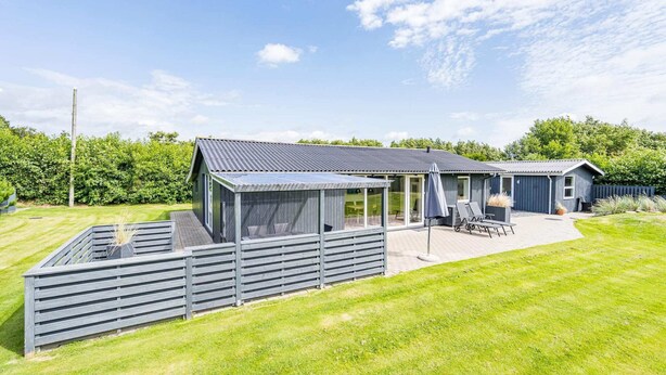 A modern house with a large deck, a covered patio, and a well-maintained lawn. - 5 Person Holiday Home in Blavand (Blavand)
