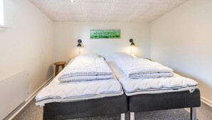A room with two beds, a small table, and a wall-mounted lamp. - 5 Person Holiday Home in Blavand (Blavand)