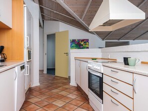 Une cuisine moderne avec des meubles blancs, une cuisinière et un four à micro-ondes. Une porte donne accès à une autre pièce.