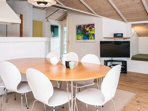 A modern dining area with a wooden table and white chairs, a painting on the wall, and a TV on a stand. - 6 Person Holiday Home in Blavand (Blavand)