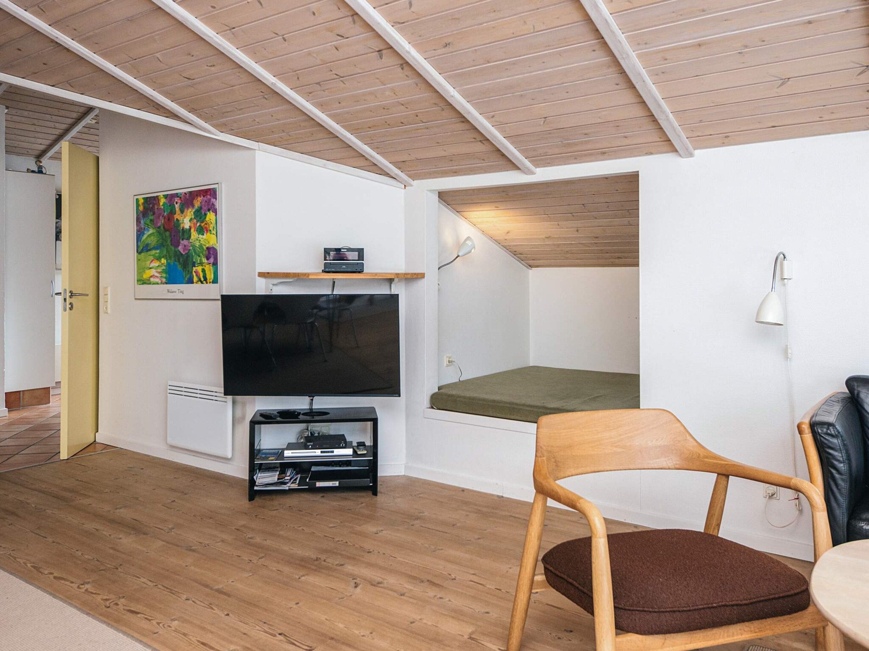 Un espacio habitable pequeño con una televisión, una pequeña estantería, una silla y una cama.