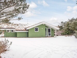 Een groene, gelijkvloerse woning met schuin dak, een veranda en een garage.