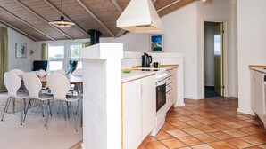 Una cocina moderna con armarios blancos, una estufa y un fregadero. Hay un comedor con sillas y una mesa.