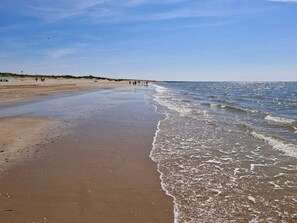 Een strand met een zandrijk strand, rustige golven en een heldere lucht.