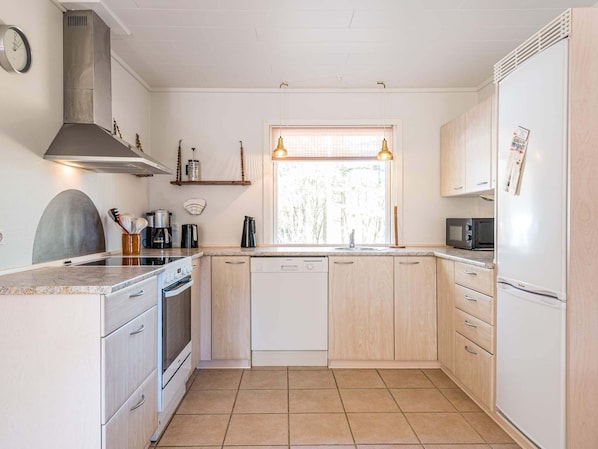 Compact kitchen with a modern design, featuring a range hood, dishwasher, microwave, and oven, and a window for natural light.