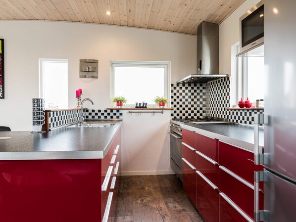 A modern kitchen with a checkered backsplash, stainless steel appliances, and a red cabinetry.