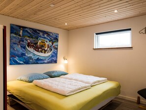 A bedroom with a bed, a painting of a boat on the wall, a window, and a wooden ceiling.