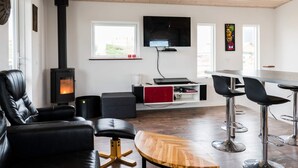 Ett modernt vardagsrum med en vedeldad kamin, möbler i läder, en tv och en barhörna.