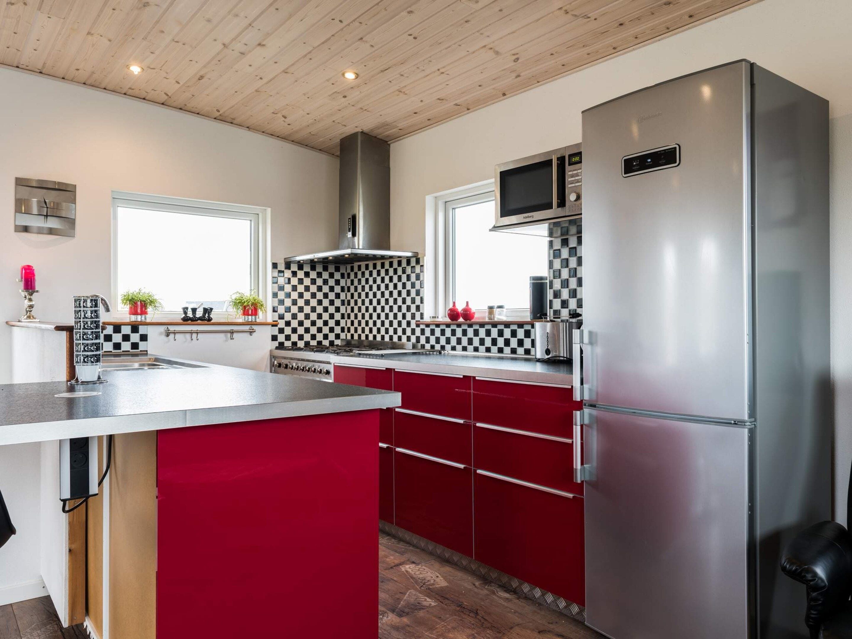 A modern kitchen with stainless steel appliances, a checkered backsplash, and red cabinetry.