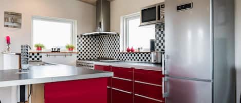 A modern kitchen with stainless steel appliances, a checkered backsplash, and red cabinetry.