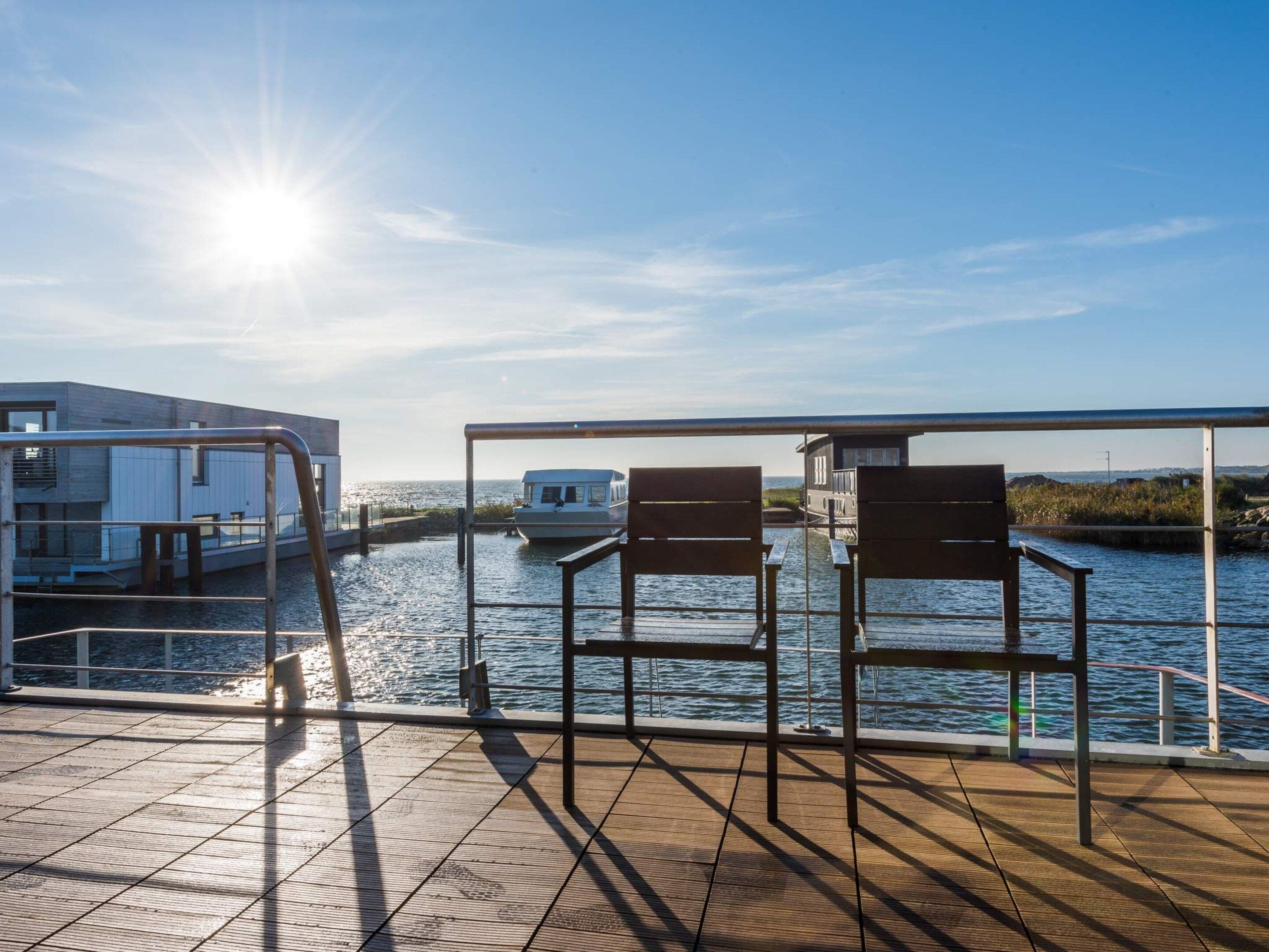A deck with a view of the water, two wooden chairs, and a railing.