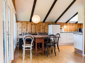 Une cuisine chaleureuse avec des murs en bois, une table à manger avec des chaises et un réfrigérateur blanc.