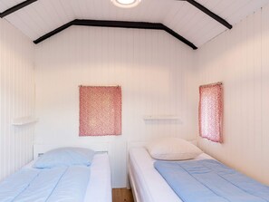 Une chambre avec deux lits, des murs blancs et un plafond en pente.
