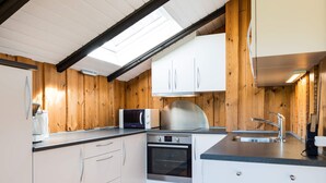 A compact kitchen with white cabinets, a microwave, a stove, and a sink. - 6 Person Holiday Home in Blavand (Blavand)