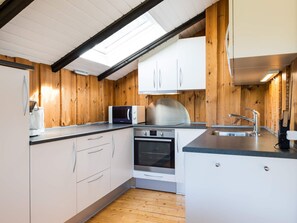 A compact kitchen with white cabinets, a microwave, a stove, and a sink. - 6 Person Holiday Home in Blavand (Blavand)