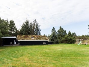 Ein Haus mit einem grünen Dach, eine kleine Gartenhütte und eine Schaukel auf einem Rasen.