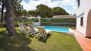 A swimming pool with lounge chairs, a tree, and a white building with a tiled roof. - Lovely Villa in Vilamoura With Private Pool (Loulé)