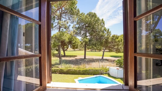 A view from a room with a large window, overlooking a swimming pool, trees, and a fenced area. - Lovely Villa in Vilamoura With Private Pool (Loulé)