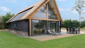 Una casa moderna con techo inclinado, grandes ventanales y un patio con mobiliario exterior.