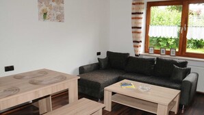 A cozy living room with a sofa, a coffee table, and a dining table. - Ferienwohnung im Bayerischen Wald mit Balkon (Drachselsried)