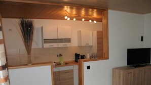 A compact kitchen with wooden cabinets, a built-in oven, and a coffee machine. - Ferienwohnung im Bayerischen Wald mit Balkon (Drachselsried)