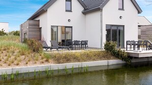 A modern two-story house with a flat roof, large sliding glass doors, and a patio with outdoor furniture. - Holiday Home Near North Sea Beach, Breeduyn (Bredene)