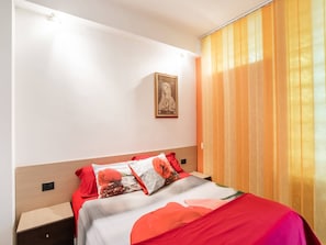 Ein Hotelzimmer mit einem Bett, einem Nachttisch, einem Wandbild und einem Fenster mit Vorhängen.