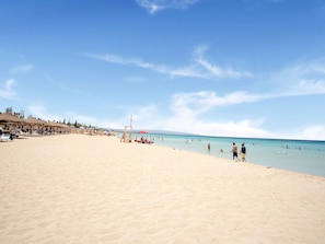 A beach with umbrellas, a lifeguard tower, and people swimming. - Simplistic Apartment in Reitani near Lido Beach (Noto)