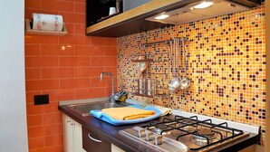 A kitchen with a gas stove, sink, and orange tiled backsplash. - Simplistic Apartment in Reitani near Lido Beach (Noto)