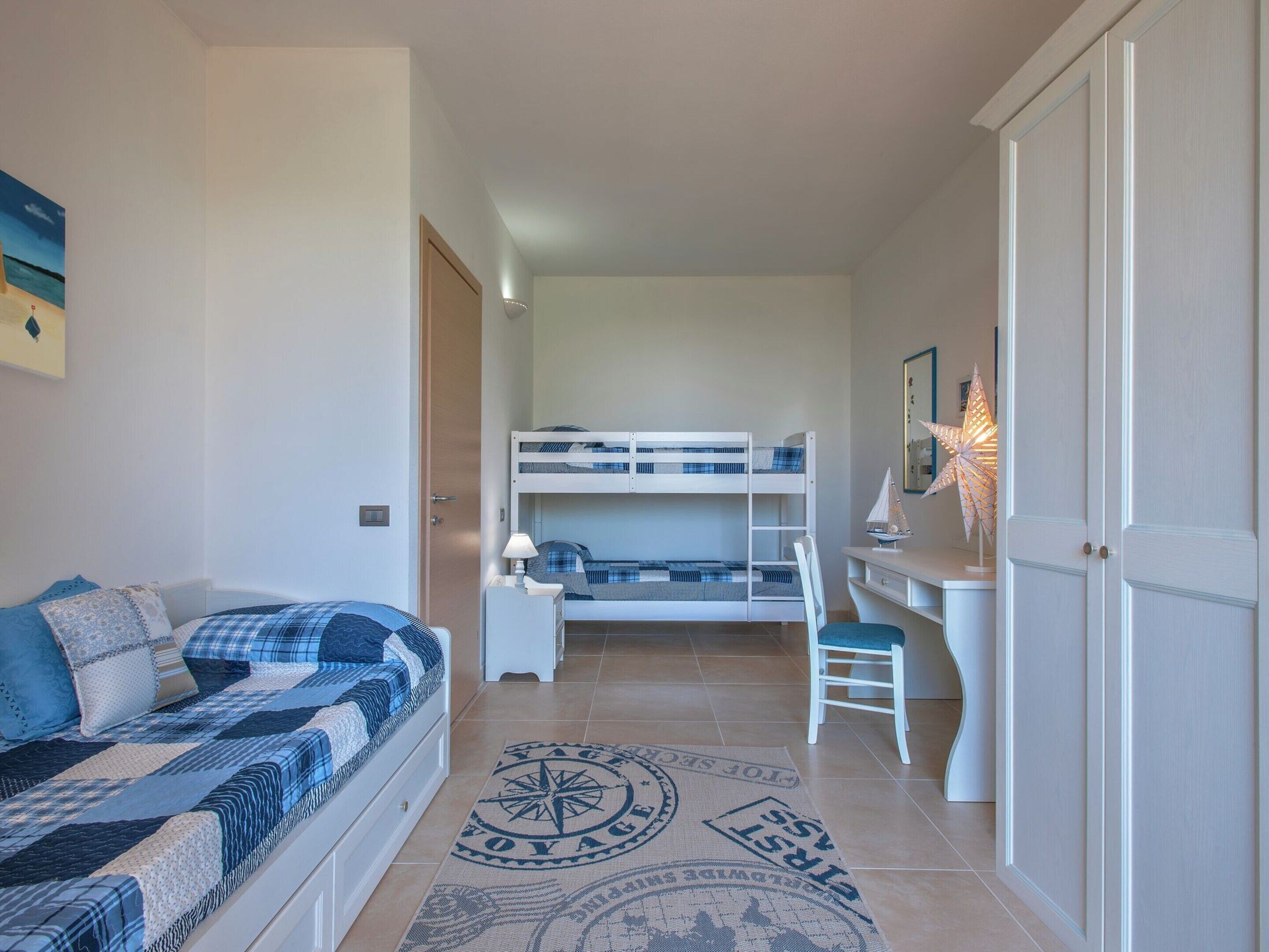 Egy hálószoba emeletes ággyal, íróasztallal, székkel, kanapéval és egy iránytű mintás szőnyeggel.