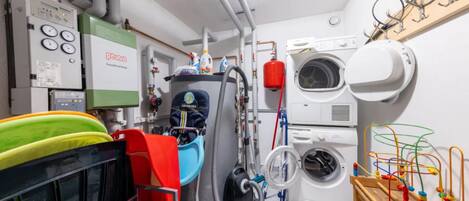 A compact kitchen with a dish rack, a washing machine, and a vacuum cleaner.