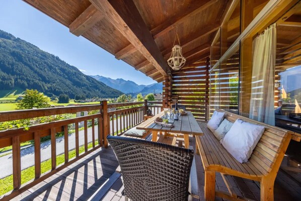 A wooden deck with a table and chairs, overlooking a mountainous landscape.