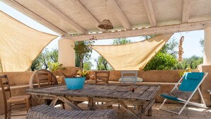 Une terrasse extérieure avec une table et des chaises en bois, un pot bleu contenant une plante et un fauteuil de jardin bleu.