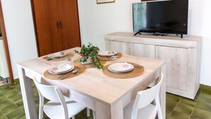 A dining area with a wooden table set for four, surrounded by white chairs. A television is mounted on a cabinet above the table. - Vue Merveilleuse Apartment (Castellammare del Golfo)