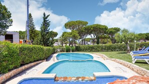A swimming pool with a stone edge, surrounded by greenery and lounge chairs. - Villa in Vilamoura With Pool Near Beach (Loulé)