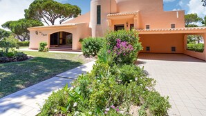 A Mediterranean-style villa with a curved facade, a covered entrance, and a well-maintained garden with various plants and flowers. - Villa in Vilamoura With Pool Near Beach (Loulé)