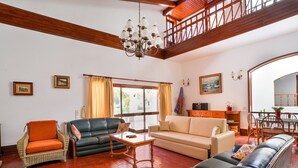 A spacious living room with a high ceiling, a dining area with a wooden table and chairs, and a balcony with a wooden railing. - Villa in Vilamoura With Pool Near Beach (Loulé)