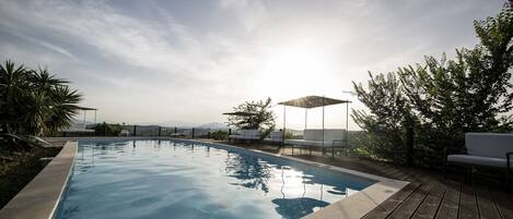 A swimming pool with a wooden deck, surrounded by greenery and a clear sky.