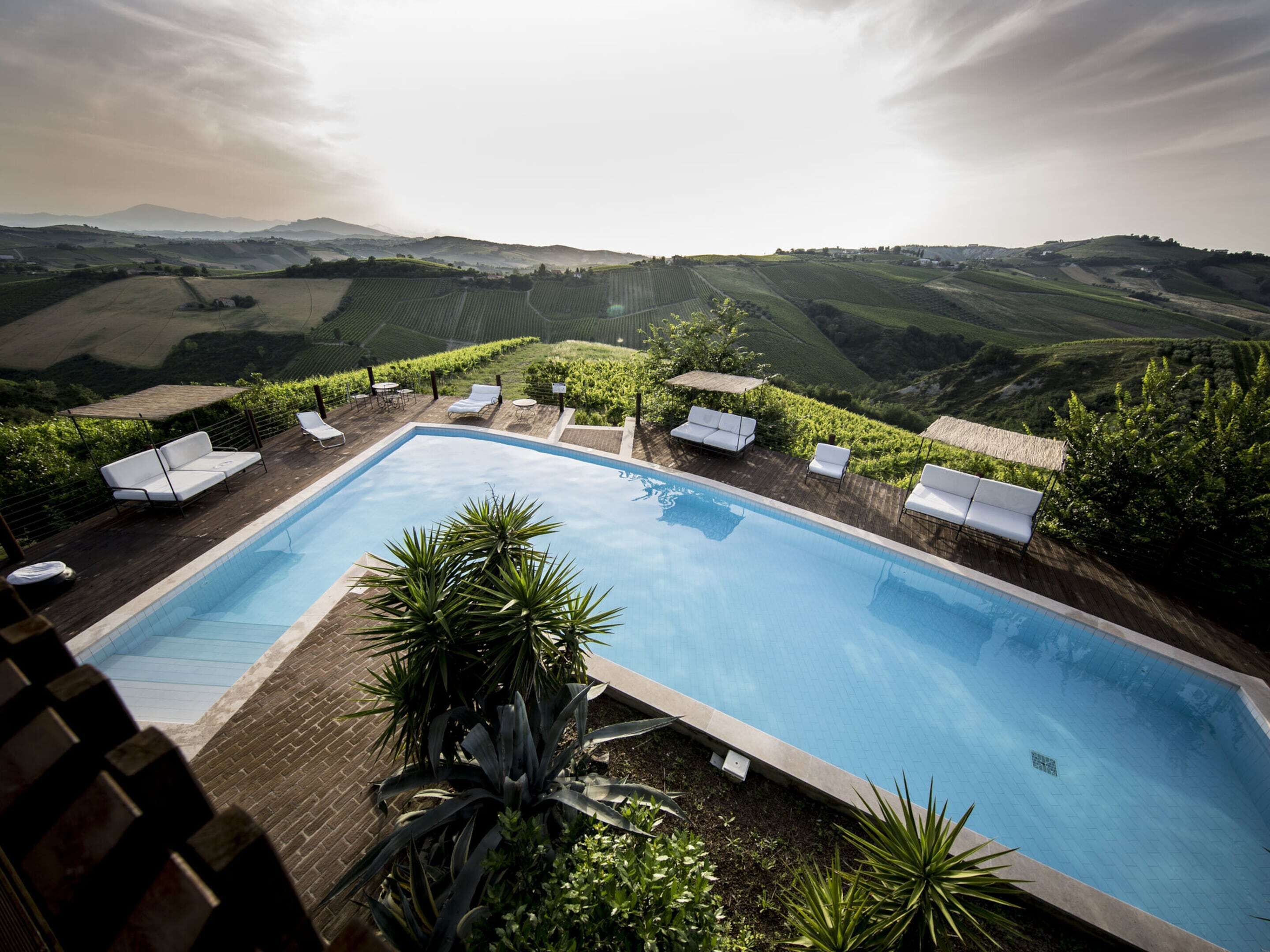 A rectangular pool with white lounge chairs and a view of rolling hills.