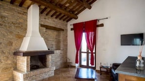 A rustic room with a stone fireplace, wooden beams, a stone wall, a red curtain, a television, and a table. - Serene Escape, Ascoli Piceno (Ripatransone)