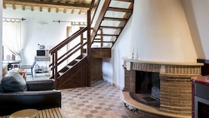 A cozy living room with a checkered floor, a fireplace, a wooden staircase, and a leather sofa. - Belvilla by Oyo Giglio (Ripatransone)