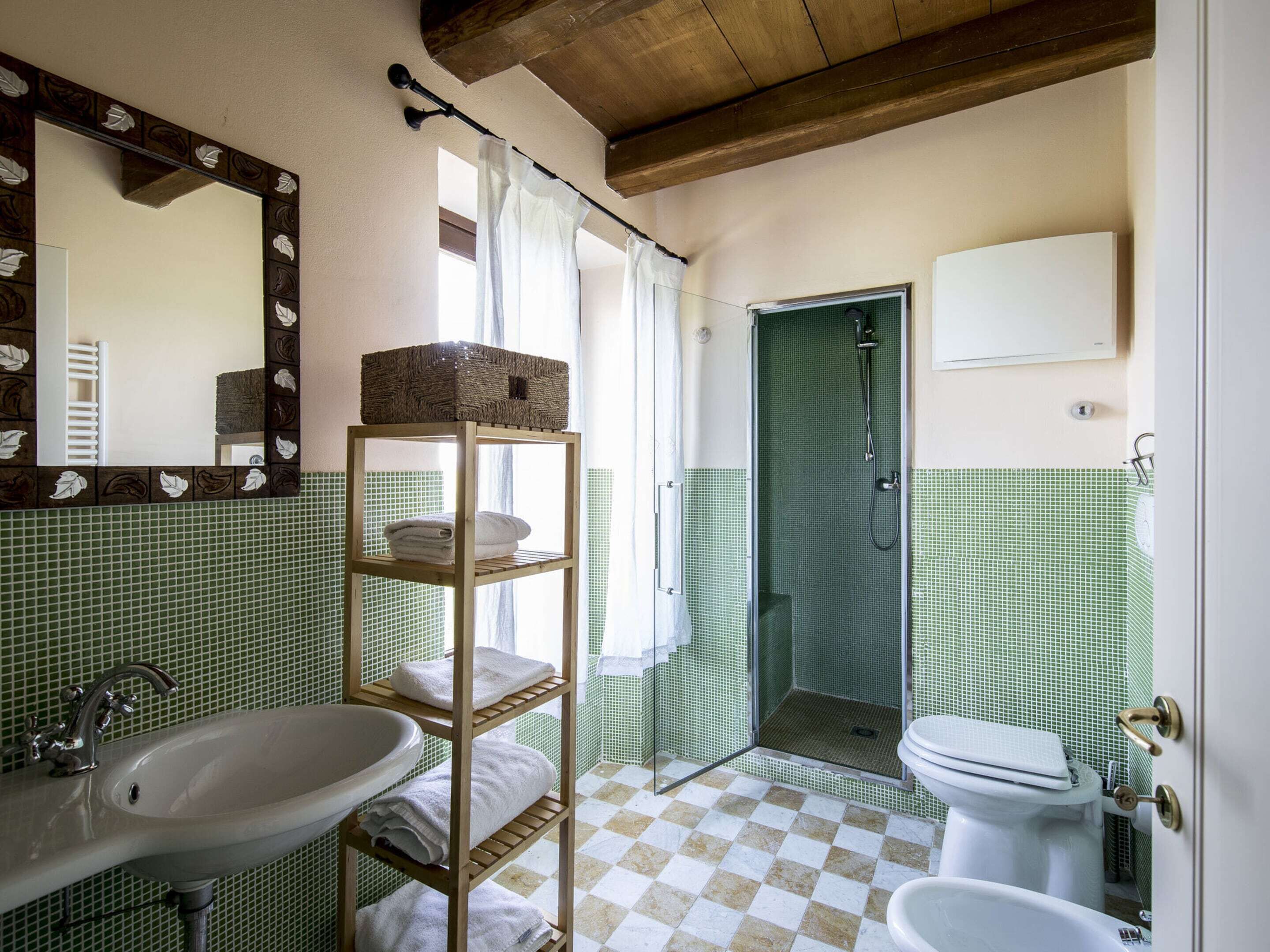 Un baño con lavamanos, un espejo con diseño de hojas, estante con toallas, ducha e inodoro.